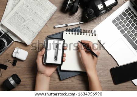Journalist with voice recorder working at wooden table, top view