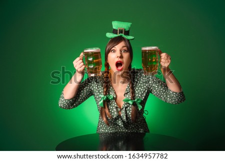 Funny young woman with beer at table against color background. St. Patrick's Day celebration