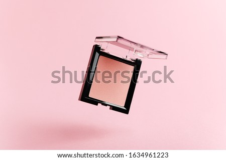 A flying packaging of pink blush on a pink background. Product of the beauty industry, female accessory of cosmetics levitate in the air. Base for makeup on the face, eyes and lips. Levitation. Royalty-Free Stock Photo #1634961223