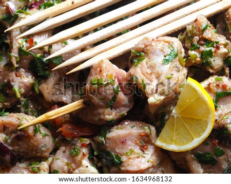 Background of juicy raw pork kebab in marinade with fresh herbs, lemon, spices and onions on a wooden skewer closeup. Picture of delicious meat for a picnic and dinner.