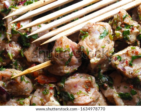 Background of juicy raw pork kebab in marinade with fresh herbs, spices and onions on a wooden skewer closeup. Picture of delicious meat for a picnic.