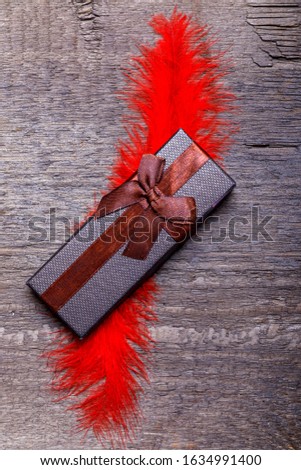 Gift box with red plume on old rustic wooden table for Valentines day. Copy space for text.