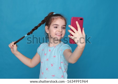 A smiling girl of eight years old holds a pink telephone in her hands on a blue background