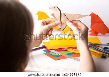 girl makes origami dinosaur of colored paper. paper, ruler, pencils, knife. interesting hobby
