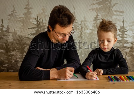 Father and son sitting at table indoors drawing with felt pens home interior. Man and kid spending leisure time together on art creative background copy space text. Happy family relations