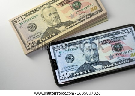 Digital and paper money. Concept photo. Pack of 50 dollar banknotes and the image of the same money on the screen of smartphone.