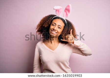 Young african american woman with afro hair wearing bunny ears over pink background smiling doing phone gesture with hand and fingers like talking on the telephone. Communicating concepts.