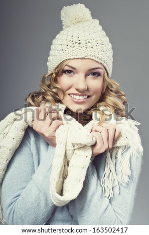 winter picture of beautiful smiling blonde woman wearing a woolen sweater and knitted scarf and cap