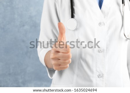 Doctor showing thumb up on blue background, closeup. Medical service