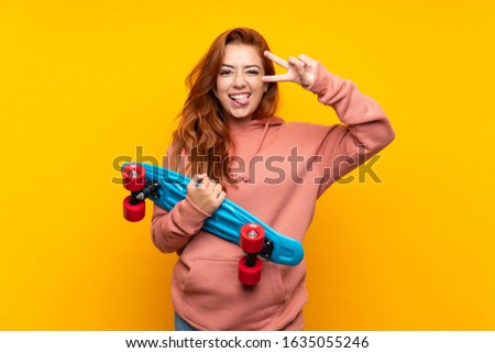 Teenager redhead girl with skate over isolated yellow background