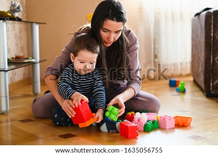 Mom and baby are playing on the floor. Beautiful baby plays with toys with happy mother indoors