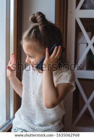 Preschooler girl talking on a cell phone and waving at the window 