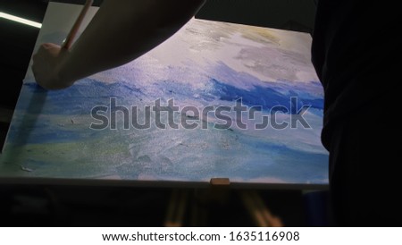 Artist copyist paint seascape with ship in ocean. Craftsman decorator draw as boat sail on blue sea with acrylic oil color. Draw finger, brush, knife palette. Canvas, easel in studio, indoor.