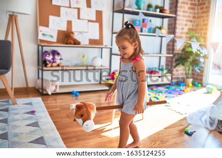 Young beautiful blonde girl kid enjoying play school with toys at kindergarten, smiling happy riding stuffed horse at home
