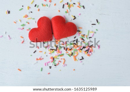 red cloth hearts on white wooden board sprinkled with color sugar rainbow decoration background.