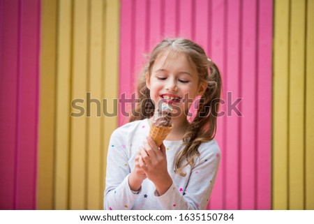 Cute little girl eating chocolate ice cream. Smiling and laughing. Colorful pink and yellow wall on background. Bright summer concept