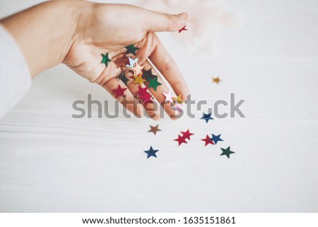 Hand holding colorful sparkling stars decorations on white background. Stylish atmospheric image. Happy birthday concept. Holiday decor. Magic in hand. Christmas