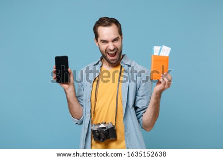 Joyful traveler tourist man in summer clothes with photo camera isolated on blue background. Passenger traveling on weekends. Air flight journey. Hold passport tickets mobile phone with empty screen