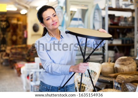 Positive woman customer standing with wooden stool in store for decor Royalty-Free Stock Photo #1635154936