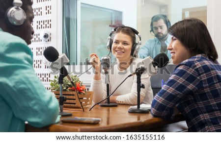 Positive international team of radio presenters interviewing guest in sound broadcasting station