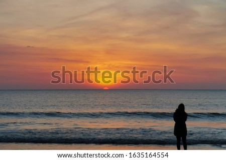 A lady, alone, trying to take a picture of the beautiful sunset on the horizon, at Tanjung Aru Beach, Sabah, Malaysia. 