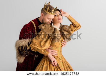king with crown hugging attractive queen isolated on grey