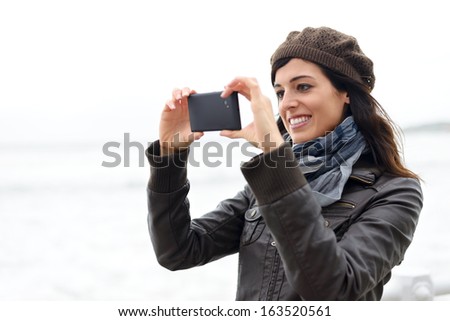 Woman taking pictures with black cellphone. Cheerful brunette using phone camera.
