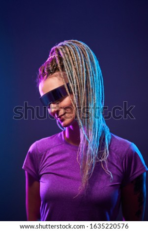 Young woman with pigtails in sunglasses looking at camera in neon light at disco