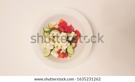 White ceramic plate with green cucumbers, red tomatoes and white cheese on a white background