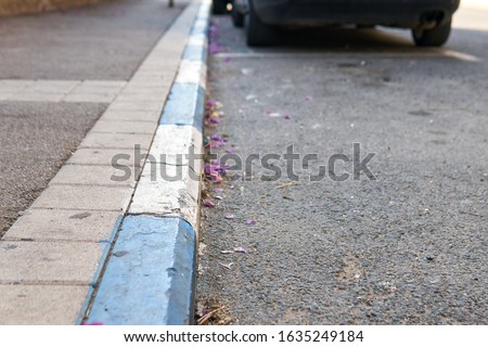 Car stands near a road curbstone painted in blue and white colors which indicate paid Parking in Israel.