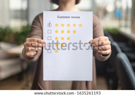 Satisfaction concept. Woman choosing with tick five star rating on paper sheet, blurred background