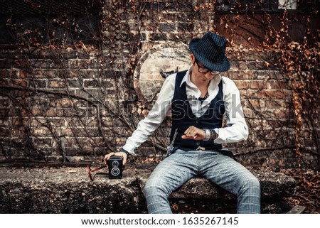 Retro-styled man with holding medium format camera and checking time on his wristwatch.