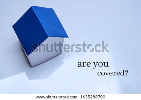 A model of a house with a classic blue roof stands on a glossy surface. Real estate insurance concept. Inscription Are you covered.