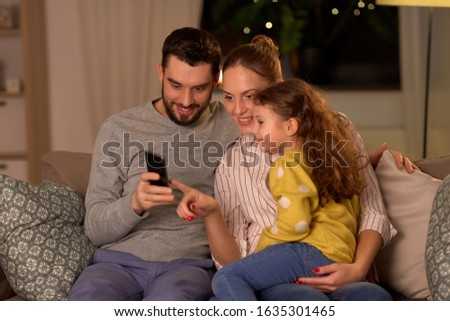 people, family and technology concept - happy mother, father and little daughter with smartphone at home at night