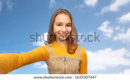 people concept - happy smiling young teenage girl taking selfie over blue sky and clouds background