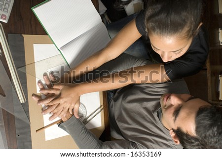 Man and woman holding hands on table. There are books and notebooks and photo taken from above. Horizontally framed photo.