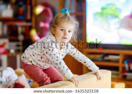 Cute little toddler girl in nightwear pajamas watching cartoons or movie on tv. Happy healthy baby child at home.