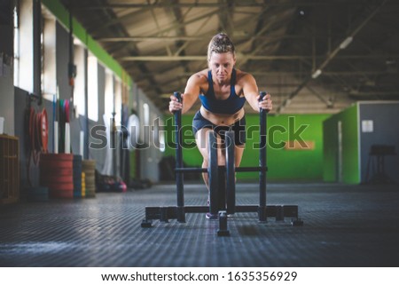 Female fitness model pushing a sled in a gym.
