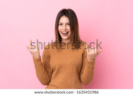 Young woman over isolated pink background making rock gesture