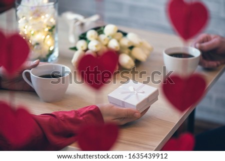 Valentines day.  Close-up of woman and man celebrating in restaurant. Boyfriend giving small box gift to girlfriend. View through a heart-shaped garland. love, romance, date