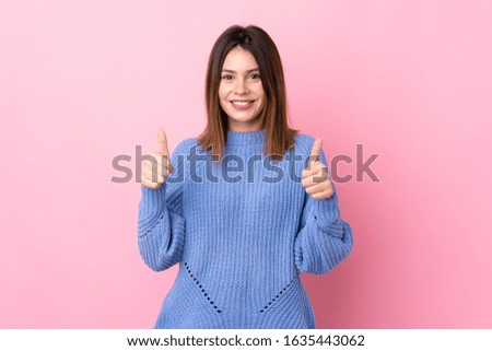 Young woman with blue sweater over isolated pink background giving a thumbs up gesture