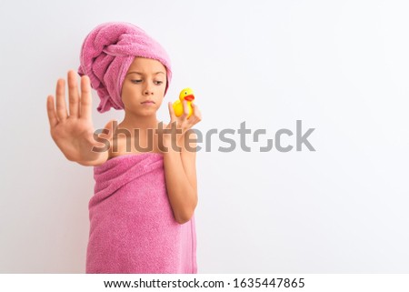 Beautiful child girl wearing shower towel holding duck over isolated white background with open hand doing stop sign with serious and confident expression, defense gesture