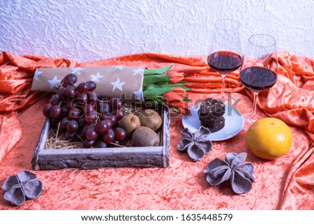 grapes, glasses with wine, tulips and nuts lie on a table on a pink background