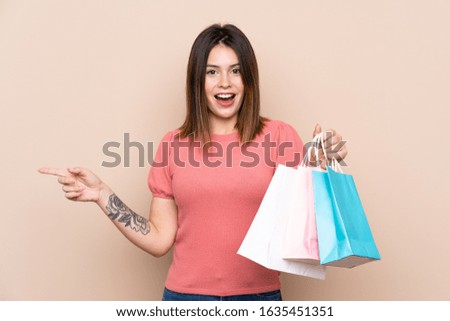 Young woman with shopping bag over isolated background surprised and pointing finger to the side