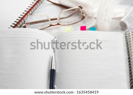 Notebook, pen, glasses, financial documents on the table. Light background.