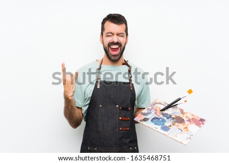Young artist man holding a palette over isolated background making rock gesture