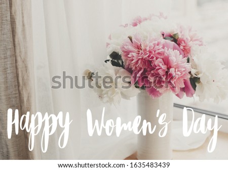 Happy Women's day text handwritten on lovely peony bouquet in sunny light on rustic  window sill. Stylish pink and white peonies in vase on wooden background. 8 march