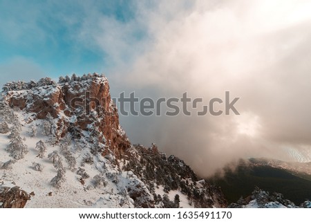 view from the cliff to a high mountain with pine trees in the clouds and the sea
