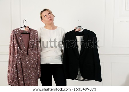 A woman has a difficult choice, not knowing what to wear. Evening dress or business suit. Nothing to wear concept. Woman chooses clothes Royalty-Free Stock Photo #1635499873