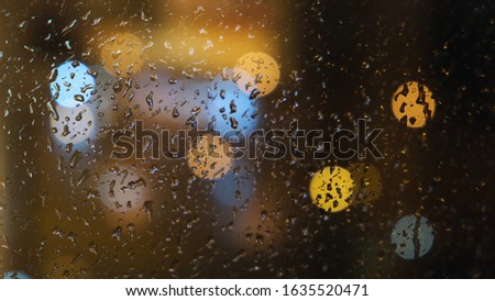 Close-up of the blurred light spots through the window and raindrops falling down on the glass at the evening. Concept. Rainy weather